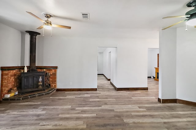 unfurnished living room with light hardwood / wood-style floors, a wood stove, and ceiling fan