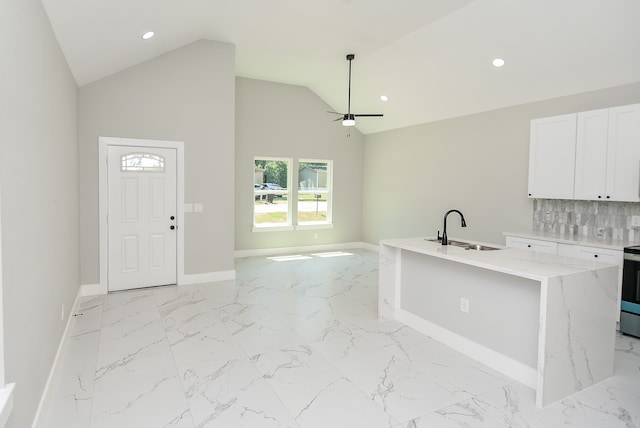 kitchen with sink, light stone counters, an island with sink, white cabinets, and backsplash