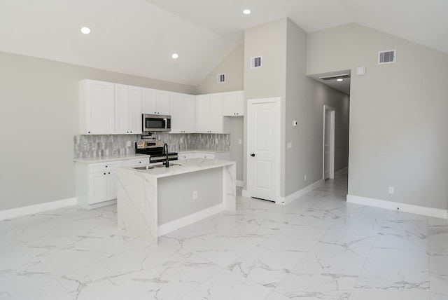 kitchen featuring tasteful backsplash, light stone counters, appliances with stainless steel finishes, an island with sink, and white cabinets