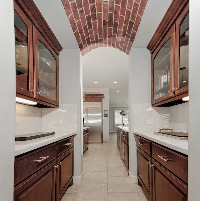 kitchen featuring built in refrigerator, backsplash, dark brown cabinetry, brick ceiling, and hanging light fixtures