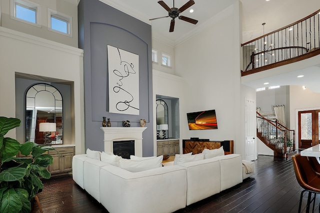 living room with ceiling fan, dark hardwood / wood-style floors, a high ceiling, and crown molding