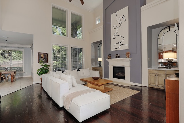 living room with dark wood-type flooring, crown molding, a towering ceiling, and ceiling fan