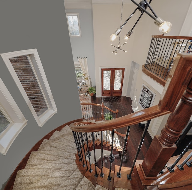 stairway with hardwood / wood-style flooring, a notable chandelier, a towering ceiling, and french doors