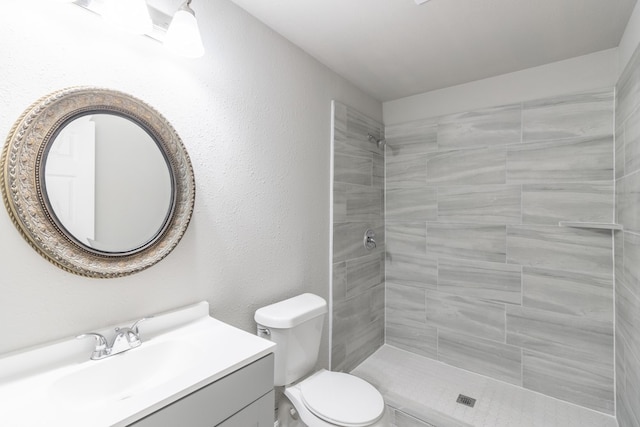 bathroom with a tile shower, vanity, and toilet