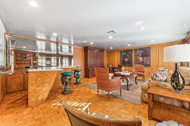 living room with light parquet flooring, wooden walls, and bar area