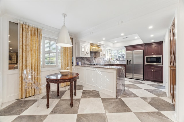 kitchen featuring tasteful backsplash, decorative light fixtures, kitchen peninsula, ornamental molding, and built in appliances