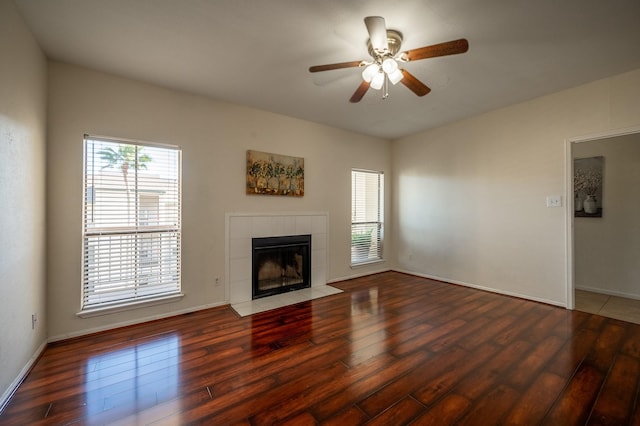 unfurnished living room featuring a tile fireplace, dark hardwood / wood-style flooring, and ceiling fan