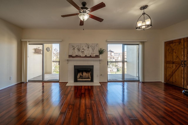 unfurnished living room featuring ceiling fan with notable chandelier, dark hardwood / wood-style floors, and a tiled fireplace