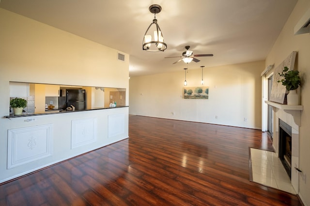 unfurnished living room featuring a tile fireplace, dark wood-type flooring, and ceiling fan with notable chandelier