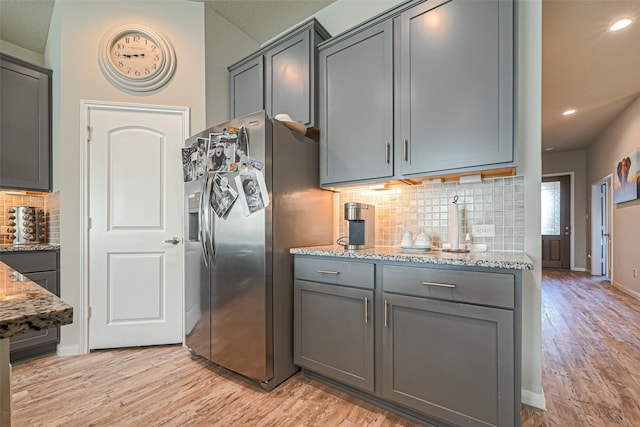 kitchen featuring light wood-type flooring, light stone counters, decorative backsplash, gray cabinetry, and stainless steel refrigerator with ice dispenser