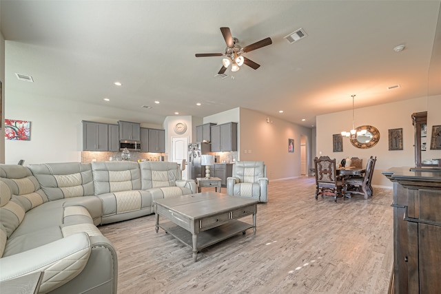 living room featuring ceiling fan with notable chandelier and light wood-type flooring