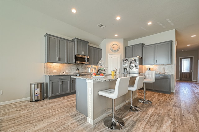 kitchen with gray cabinetry, light hardwood / wood-style flooring, a center island with sink, stainless steel appliances, and a breakfast bar