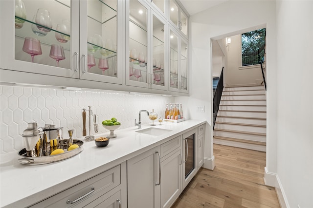 bar featuring light wood-type flooring, decorative backsplash, and sink