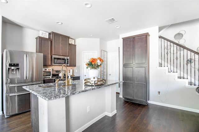 kitchen with stainless steel appliances, dark stone counters, and a kitchen island with sink