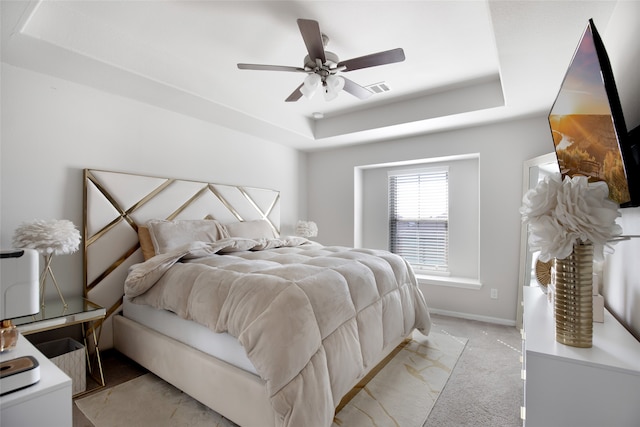 carpeted bedroom with ceiling fan and a raised ceiling