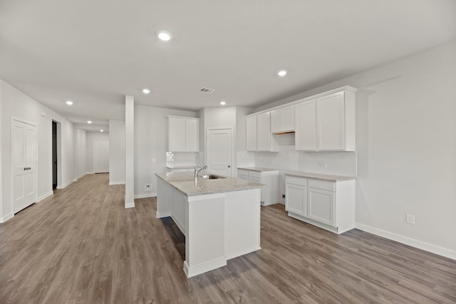 kitchen featuring a kitchen island with sink, white cabinets, sink, light wood-type flooring, and light stone counters