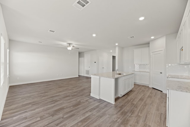 kitchen featuring white cabinets, decorative backsplash, a center island with sink, and light wood-type flooring