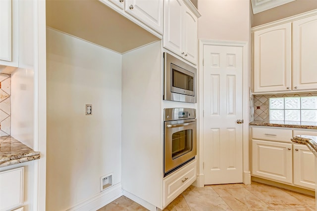 kitchen with light tile patterned flooring, stone countertops, tasteful backsplash, appliances with stainless steel finishes, and white cabinetry