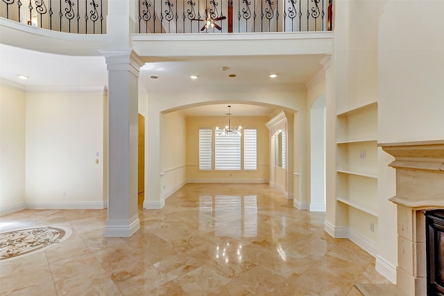 unfurnished living room featuring ornate columns, a high ceiling, a notable chandelier, a high end fireplace, and built in shelves