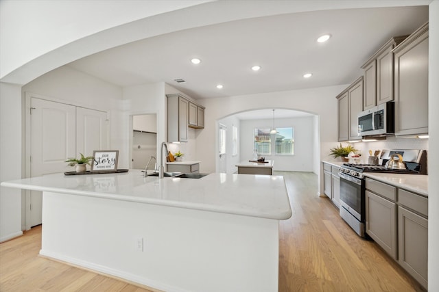 kitchen featuring sink, a kitchen island with sink, gray cabinets, stainless steel appliances, and light hardwood / wood-style floors