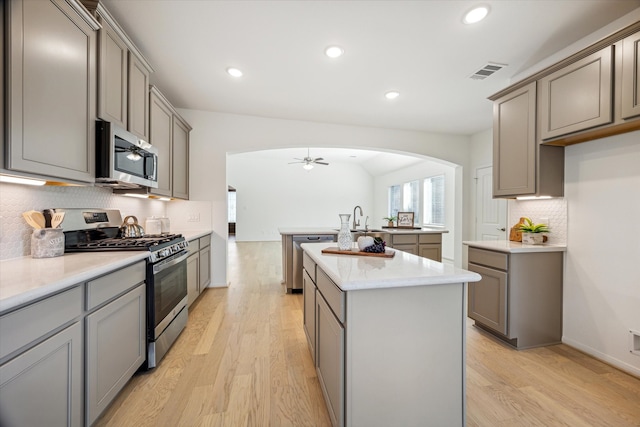 kitchen with gray cabinetry, a center island with sink, light hardwood / wood-style flooring, appliances with stainless steel finishes, and vaulted ceiling