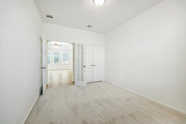 unfurnished bedroom featuring a closet, french doors, and light colored carpet