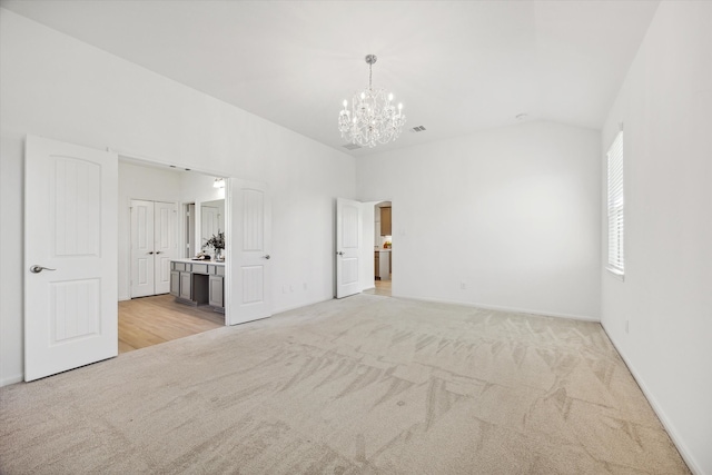 spare room featuring light carpet, an inviting chandelier, and lofted ceiling