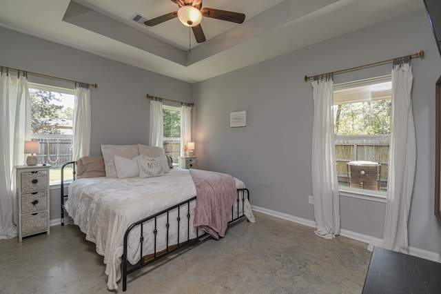 bedroom with multiple windows, ceiling fan, a raised ceiling, and concrete flooring