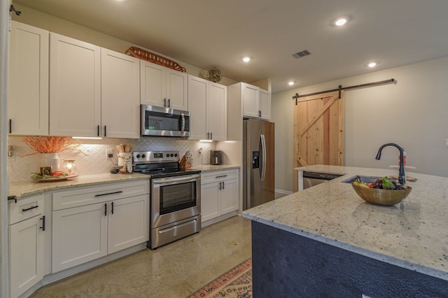 kitchen with light stone counters, white cabinets, stainless steel appliances, and a barn door