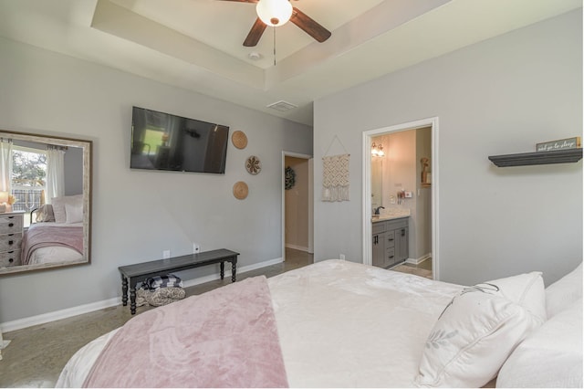 carpeted bedroom featuring a raised ceiling, ensuite bathroom, and ceiling fan