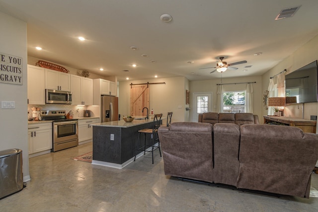 living room with ceiling fan, a barn door, sink, and concrete flooring