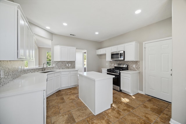 kitchen with white cabinets, sink, backsplash, appliances with stainless steel finishes, and a center island