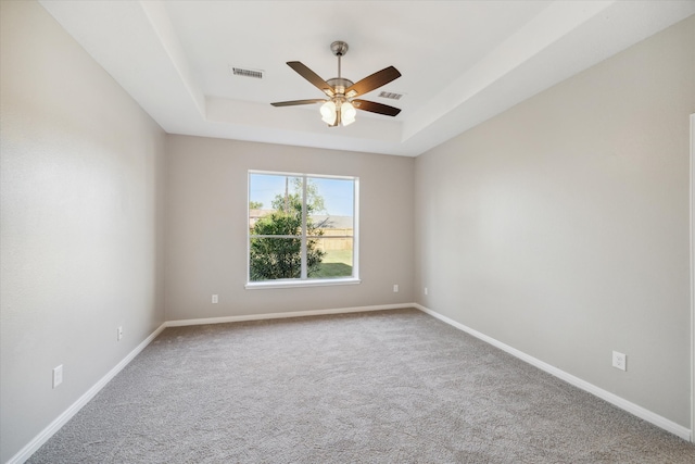 empty room with a raised ceiling, carpet, and ceiling fan