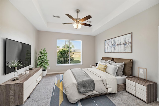 bedroom with ceiling fan, a raised ceiling, and light carpet