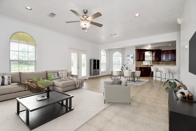 tiled living room with ceiling fan, sink, and ornamental molding