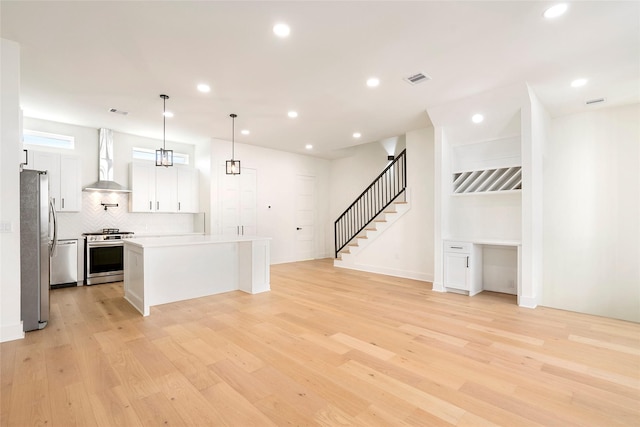 kitchen with white cabinetry, light hardwood / wood-style flooring, wall chimney exhaust hood, and appliances with stainless steel finishes