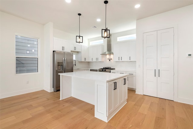 kitchen featuring a center island, white cabinets, wall chimney range hood, appliances with stainless steel finishes, and light hardwood / wood-style floors