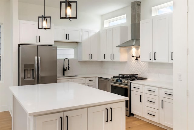 kitchen featuring appliances with stainless steel finishes, sink, wall chimney range hood, decorative light fixtures, and white cabinetry