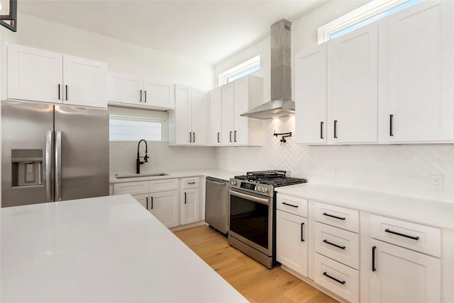 kitchen with stainless steel appliances, sink, wall chimney range hood, light hardwood / wood-style flooring, and white cabinetry