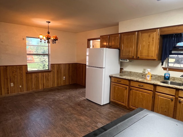 kitchen with dark hardwood / wood-style flooring, white fridge, a notable chandelier, wood walls, and decorative light fixtures