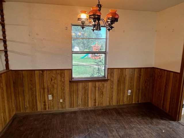 unfurnished dining area featuring an inviting chandelier, wood walls, and dark hardwood / wood-style flooring