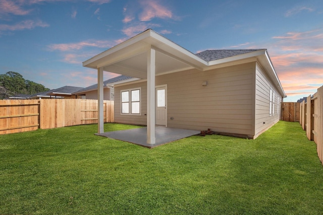 back house at dusk with a patio area and a lawn