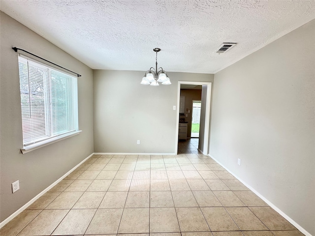 empty room featuring an inviting chandelier, light tile patterned floors, and a textured ceiling