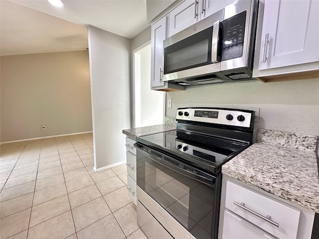 kitchen with light stone counters, light tile patterned flooring, lofted ceiling, white cabinetry, and appliances with stainless steel finishes