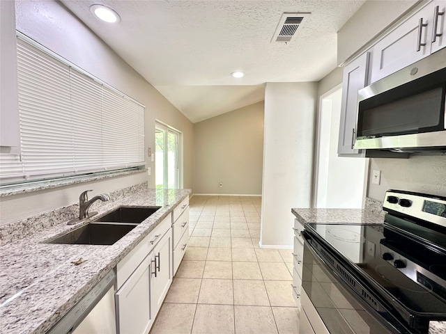 kitchen with vaulted ceiling, sink, stainless steel appliances, white cabinets, and light tile patterned floors