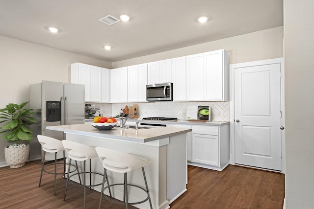 kitchen featuring a breakfast bar area, stainless steel appliances, visible vents, backsplash, and dark wood-type flooring