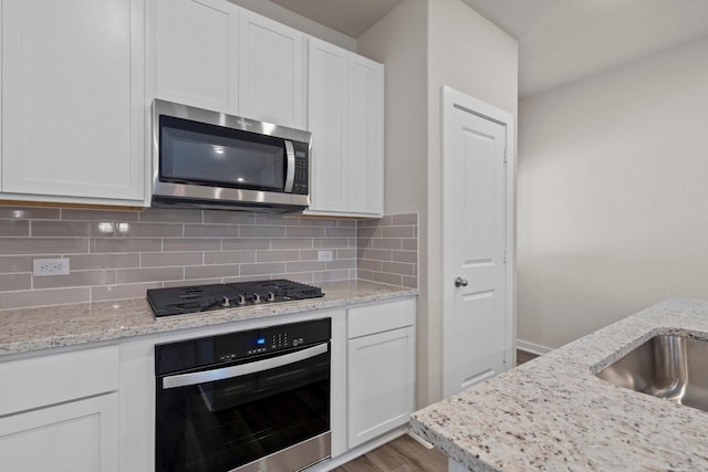 kitchen featuring tasteful backsplash, stainless steel appliances, white cabinetry, and light stone counters