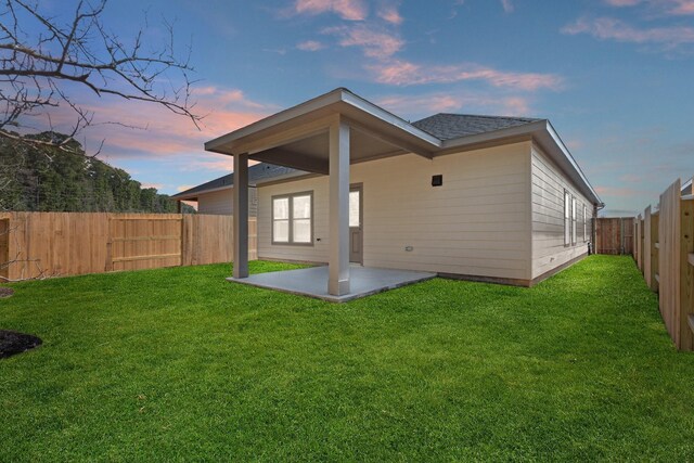 back house at dusk featuring a patio area and a lawn