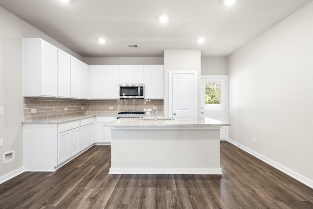 kitchen featuring light stone counters, a kitchen island with sink, and white cabinets