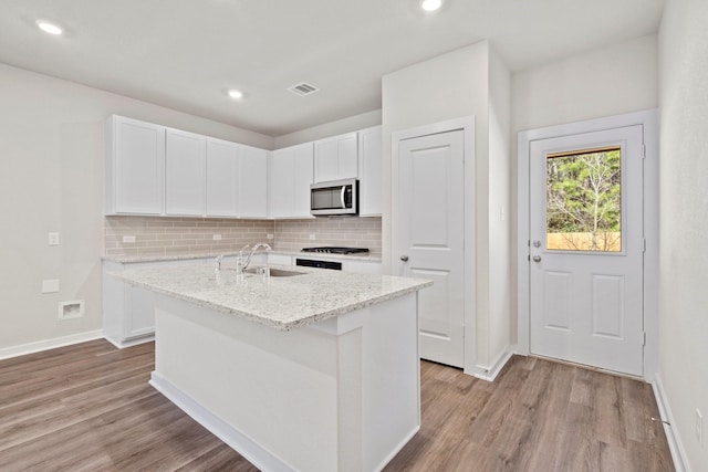 kitchen with white cabinetry, a center island with sink, sink, light stone counters, and decorative backsplash